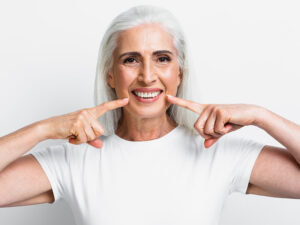 mulher idosa sorrindo e apontando pro sorriso